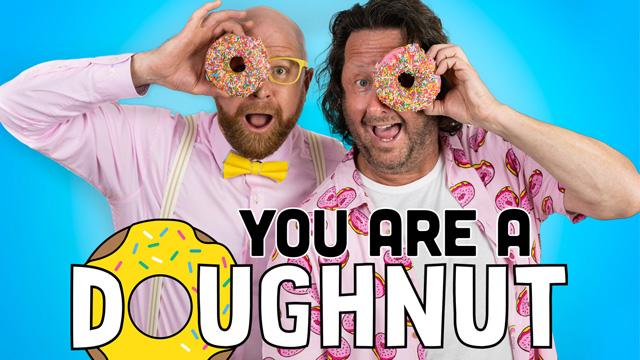Two men in colourful clothes holding doughnuts in front of their faces and laughing