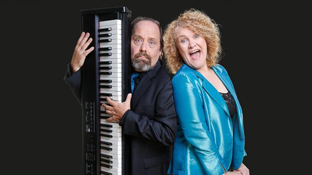 Man holding a piano keyboard alongside his face and a woman with curly blonde hair making an excited laughing face