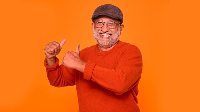 Senior man in orange sweater smiling against orange background