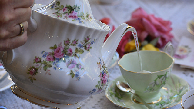 Close up of person pouring tea out of a fancy china teapot