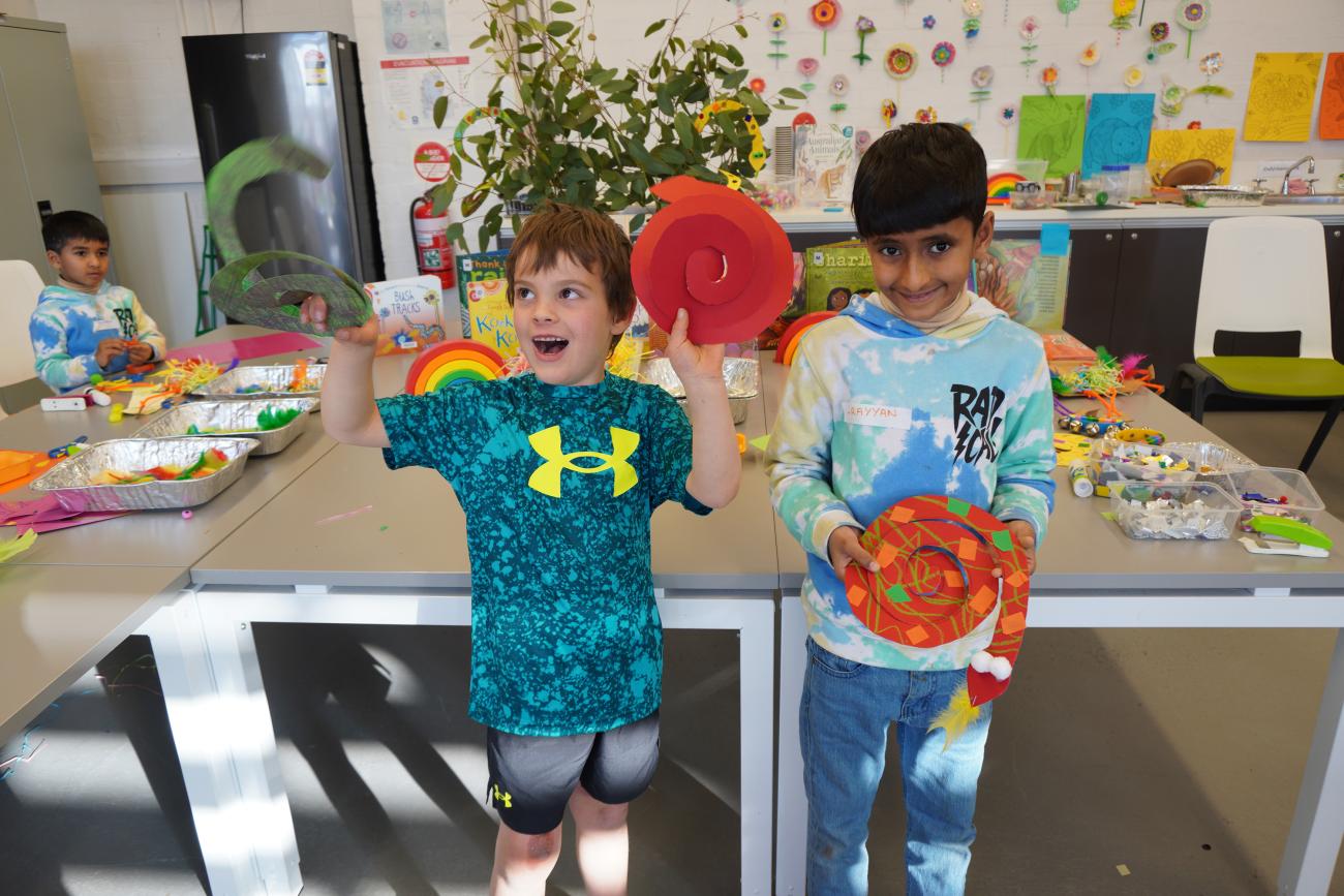 Two kids holding up their artwork and smiling