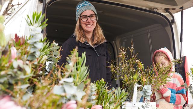 Woman wearing a beanie, standing behind a table of flower arrangements