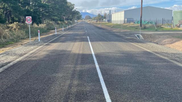 Long shot of a newly-sealed rural road, with trees alongside the roadway's edge