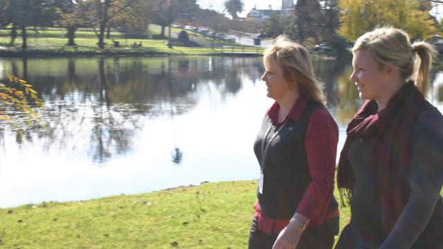 Two people walking alongside Alexandra Lake on a sunny morning