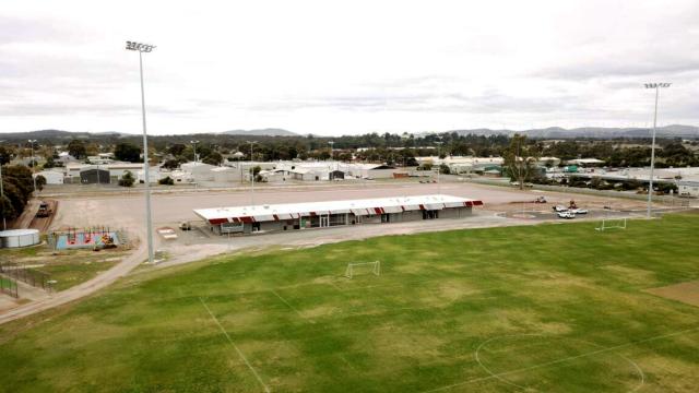 Long shot of a sporting pavilion with stadium lights, and large section of a grassy AFL playing field