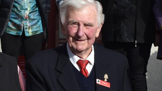 Man with white hair and a navy suit at a Council event, smiling at camera