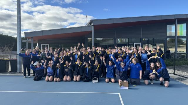 A group of 70 high school students outdoors, waving their hands in the air and smiling