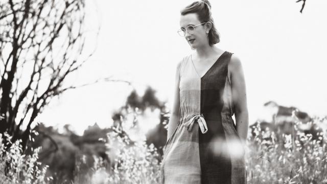 Black and white image of young woman walking through grassy parkland