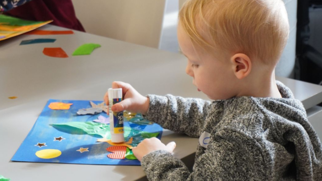 Young child doing an art class with coloured paper and glue at a table