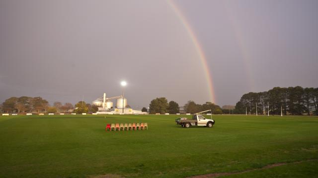 A sports oval in the twilight with a large rainbow curving over the grass and a vehicle closer to the foreground