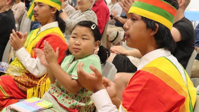 Two young men in traditional dress with young girl, all are clapping while watching a performance