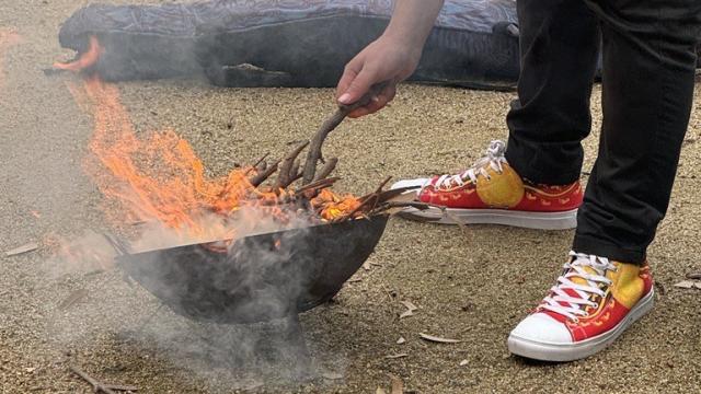 Close-up of a man in sneakers printed with the Aboriginal flag, stoking a fire for a smoking ceremony