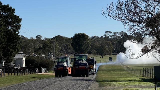 Roadworks vehicles driving along a freshly-sealed rural road