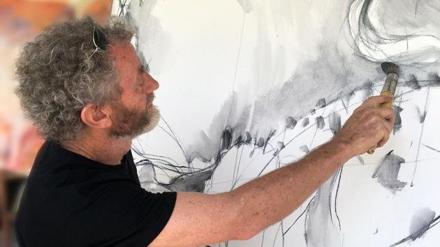 A man with curly grey hair painting on a canvas