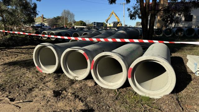 Large diameter concrete pipes laid in a row next to a freshly-dug roadside ditch