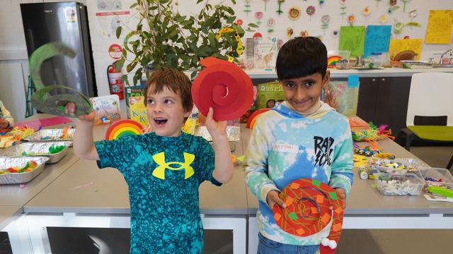 Two children smiling sweetly and holding their artwork for the camera