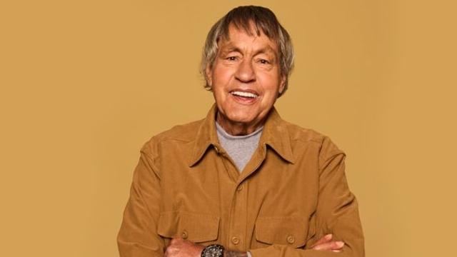 Senior man in a brown jacket smiling with arms crossed