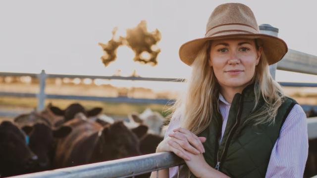 Young woman in akubra hat standing in front of pen of cattle
