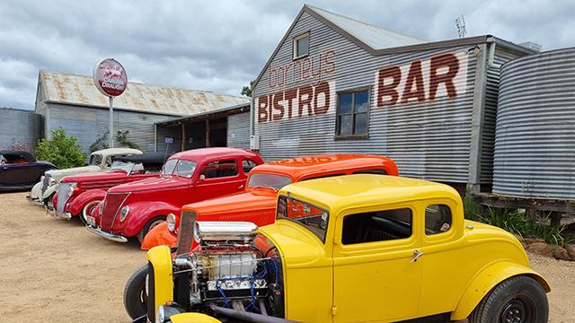 Four brightly coloured vintage cars parked outside a rural pub