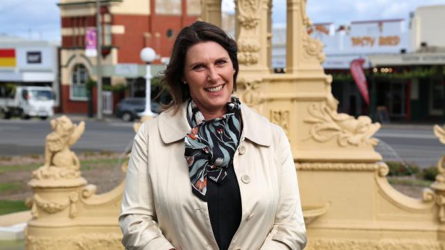 A lady in a casual professional outfit smiling while standing in front of a large elegant fountain