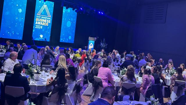 Large audience seated at dinner tables inside decorated auditorium