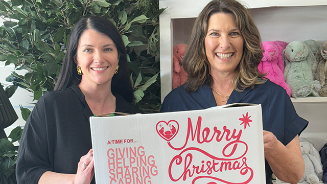 Two women smiling and holding a carboard box which says Merry Christmas on it