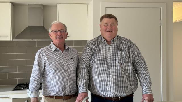 Two men smiling and standing inside the kitchen of a new house