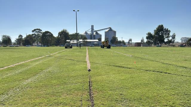A large grassy field with a long, straight trench dug into it.