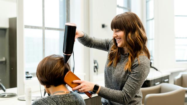 A hairdresser is blow drying a client's hair in a salon