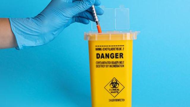 A gloved hand is disposing of a needle