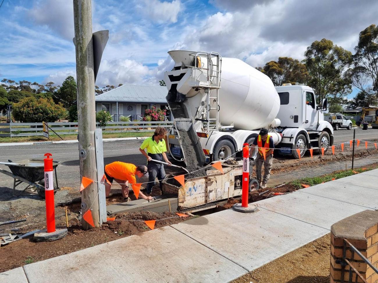 Fresh concrete poured on a street's kerb and channel with orange construction flags