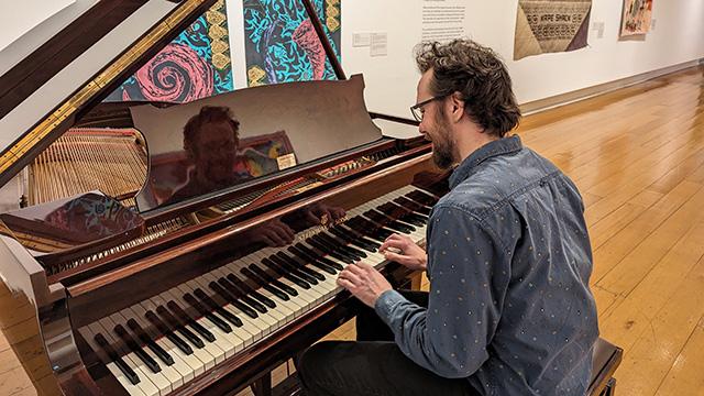 Young man playing a grand piano inside a gallery space