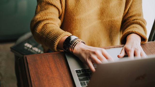 A person in a mustard-coloured jumper typing on a laptop