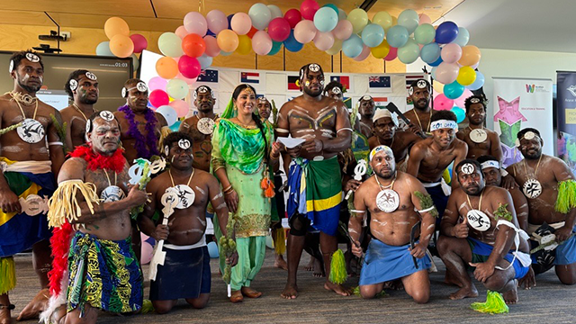 A group of men in traditional Solomon Islands dancing costumes with a lady in traditional Punjabi dress