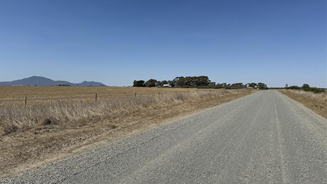 Long shot of a rural road which has been freshly sealed. Sunny day with blue skies