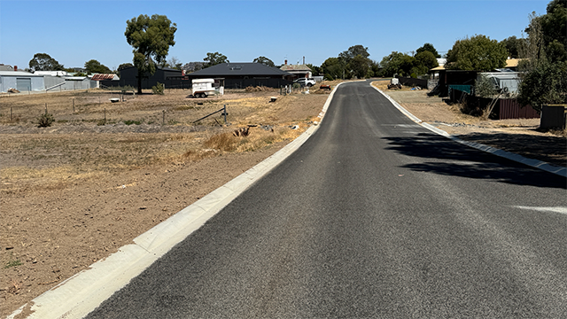 Long shot of a newly-sealed rural road on a bright sunny day with blue sky