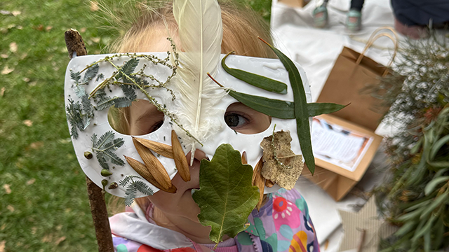Toddler child wearing a mask made of gum leaves, gumnuts and other bits of nature