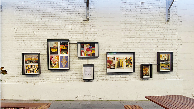 Outdoor gallery space with artworks hung on a white brick wall