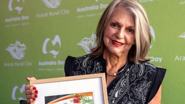An older lady smiling while holding a framed certificate