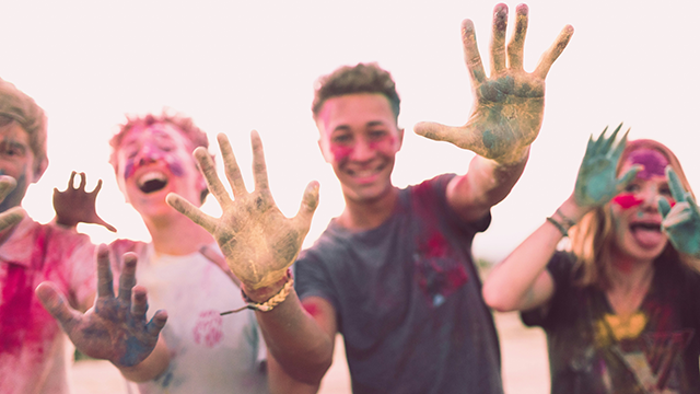 A group of teenagers daubed in rainbow coloured powder laughing and holding their hands up to the camera